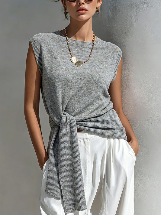 Woman wearing a gray sleeveless top with a knot detail and white pants against a neutral background