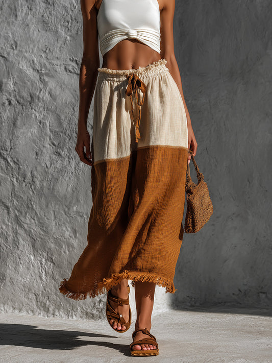 Woman wearing a two-tone skirt with a white top against a gray wall.