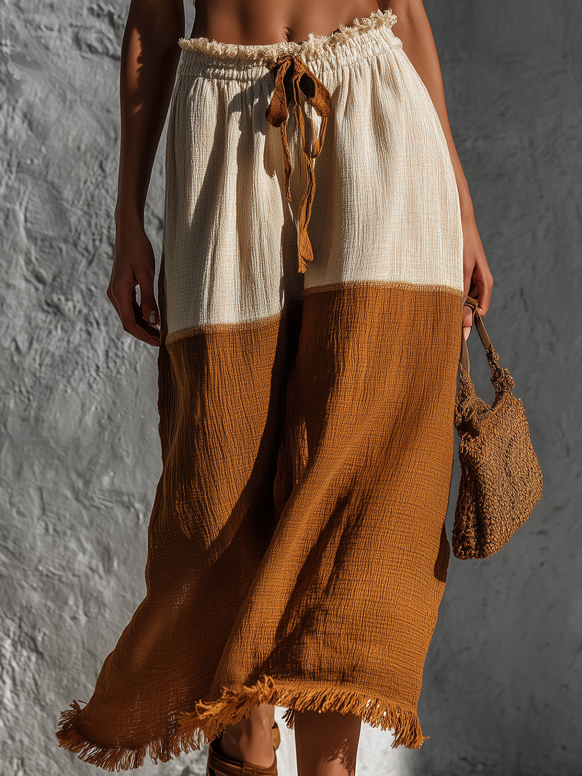Person wearing a two-tone skirt with white top and brown bottom, holding a matching bag against a textured gray background.