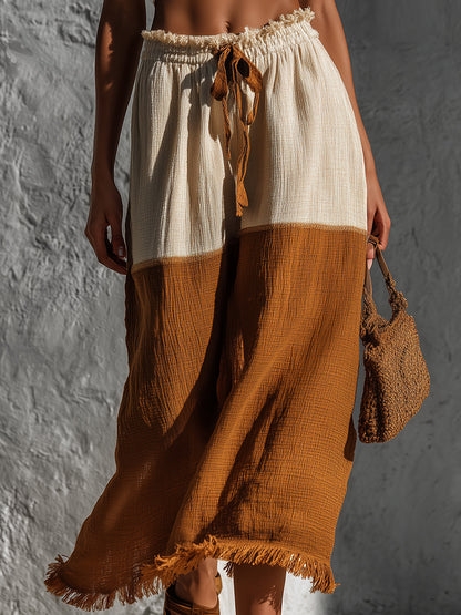 Person wearing a two-tone skirt with white top and brown bottom, holding a matching bag against a textured gray background.