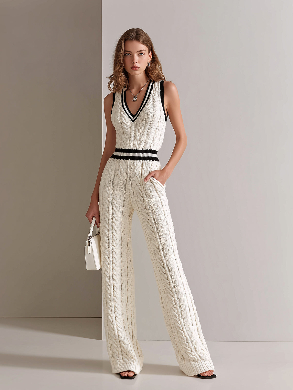 Woman wearing a white cable knit jumpsuit with black accents against a neutral background