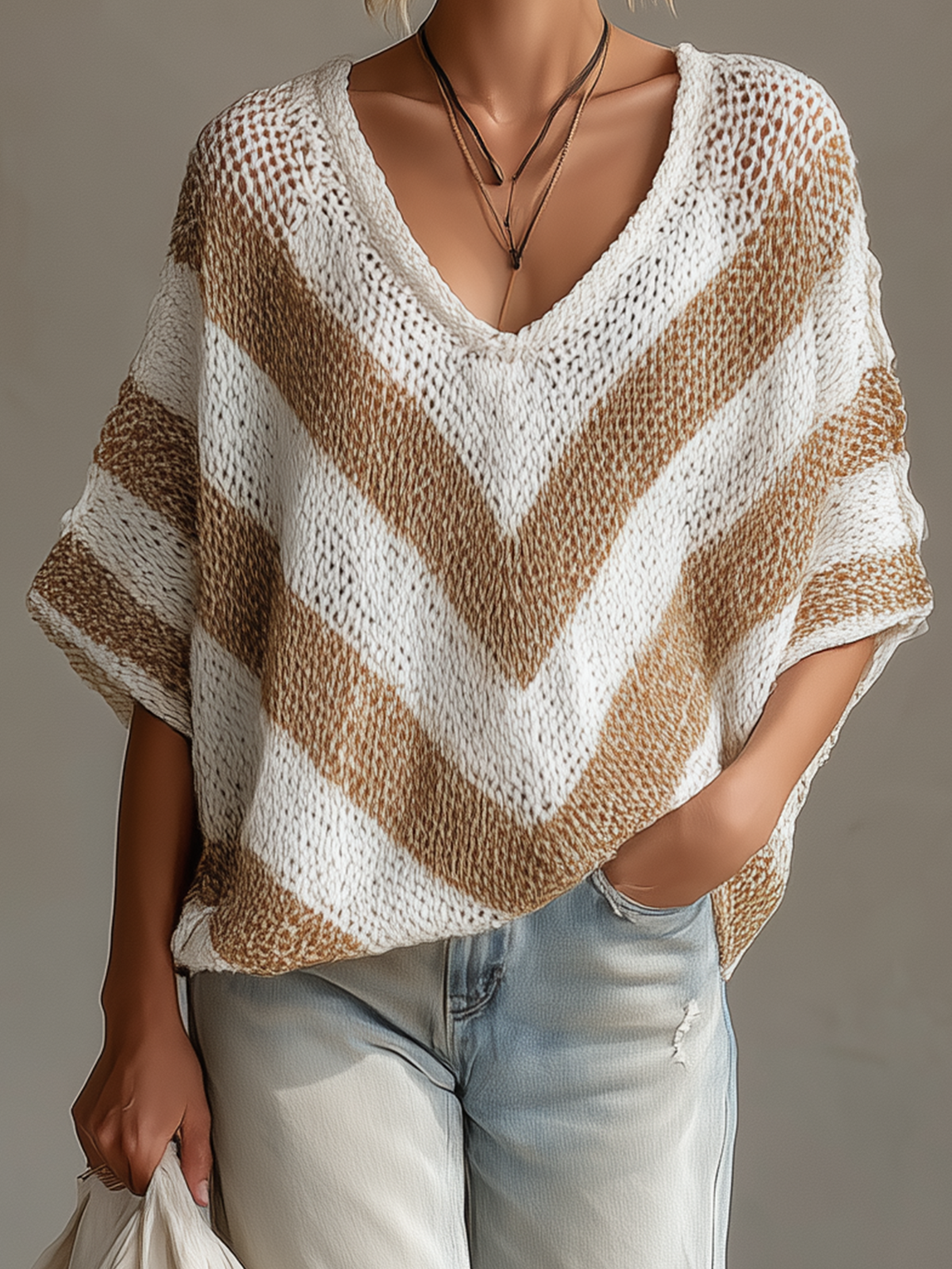 Person wearing a beige and white striped knit poncho with light blue jeans on a neutral background