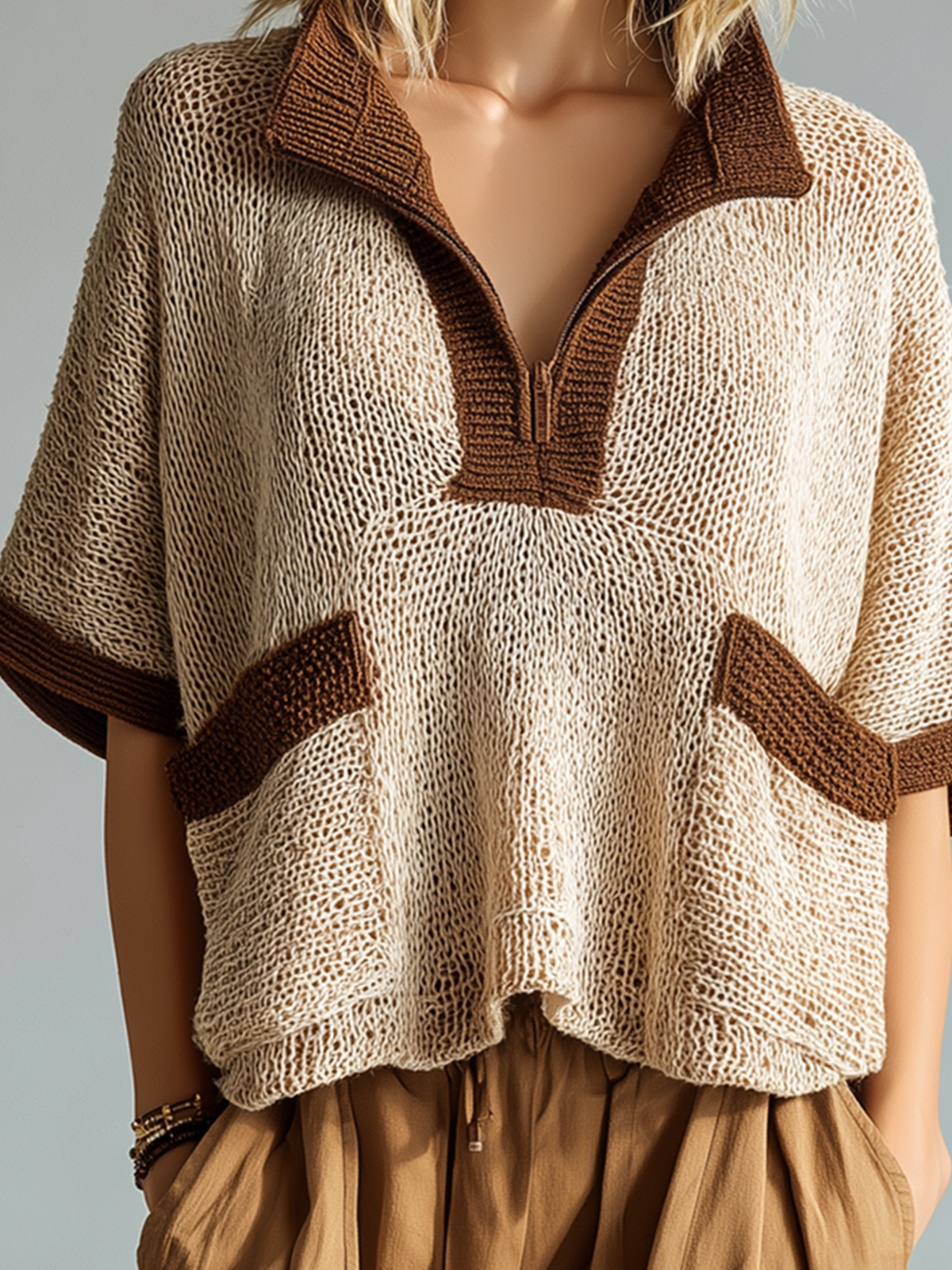 Knitted poncho with brown trim worn by a mannequin against a neutral background