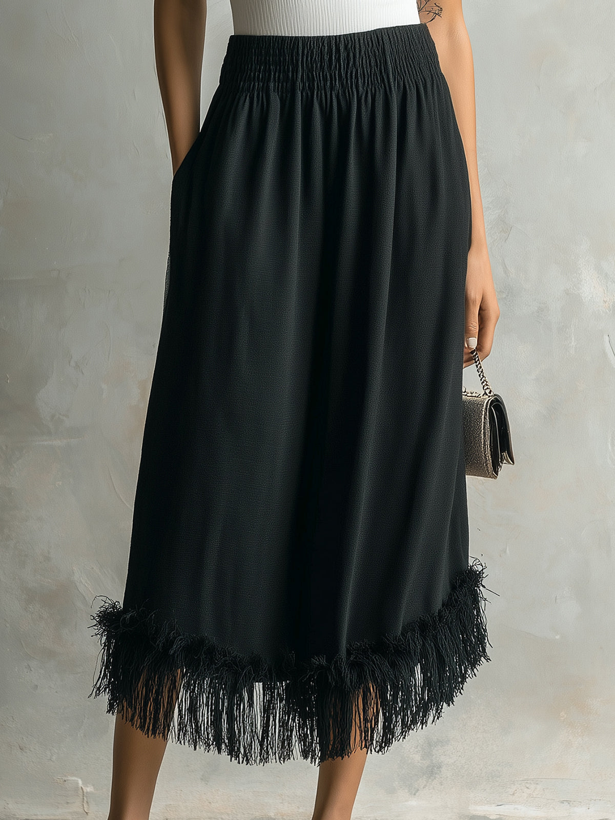 Black fringed skirt worn by a person on a neutral background