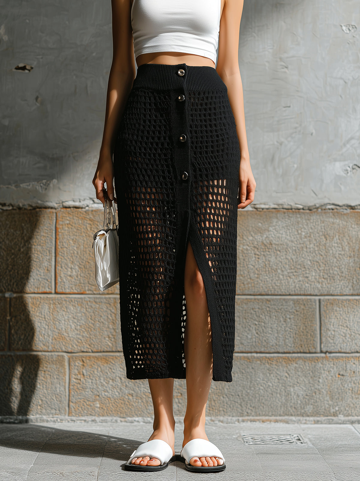 Person wearing a black crochet skirt with a white top against a gray wall.