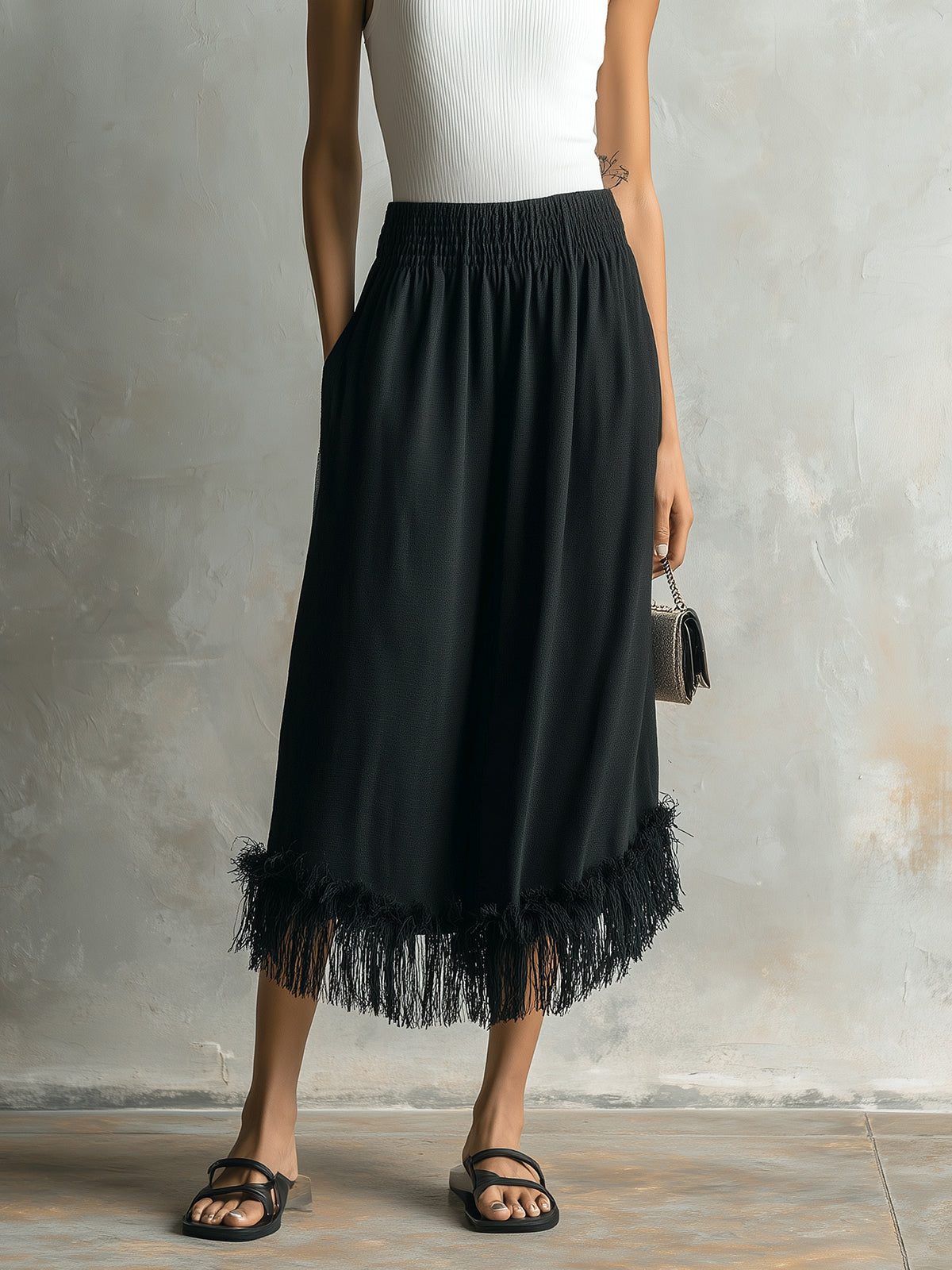 Person wearing a black skirt with fringe details against a gray background