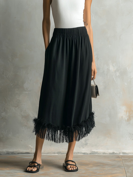 Person wearing a black skirt with fringe details against a gray background